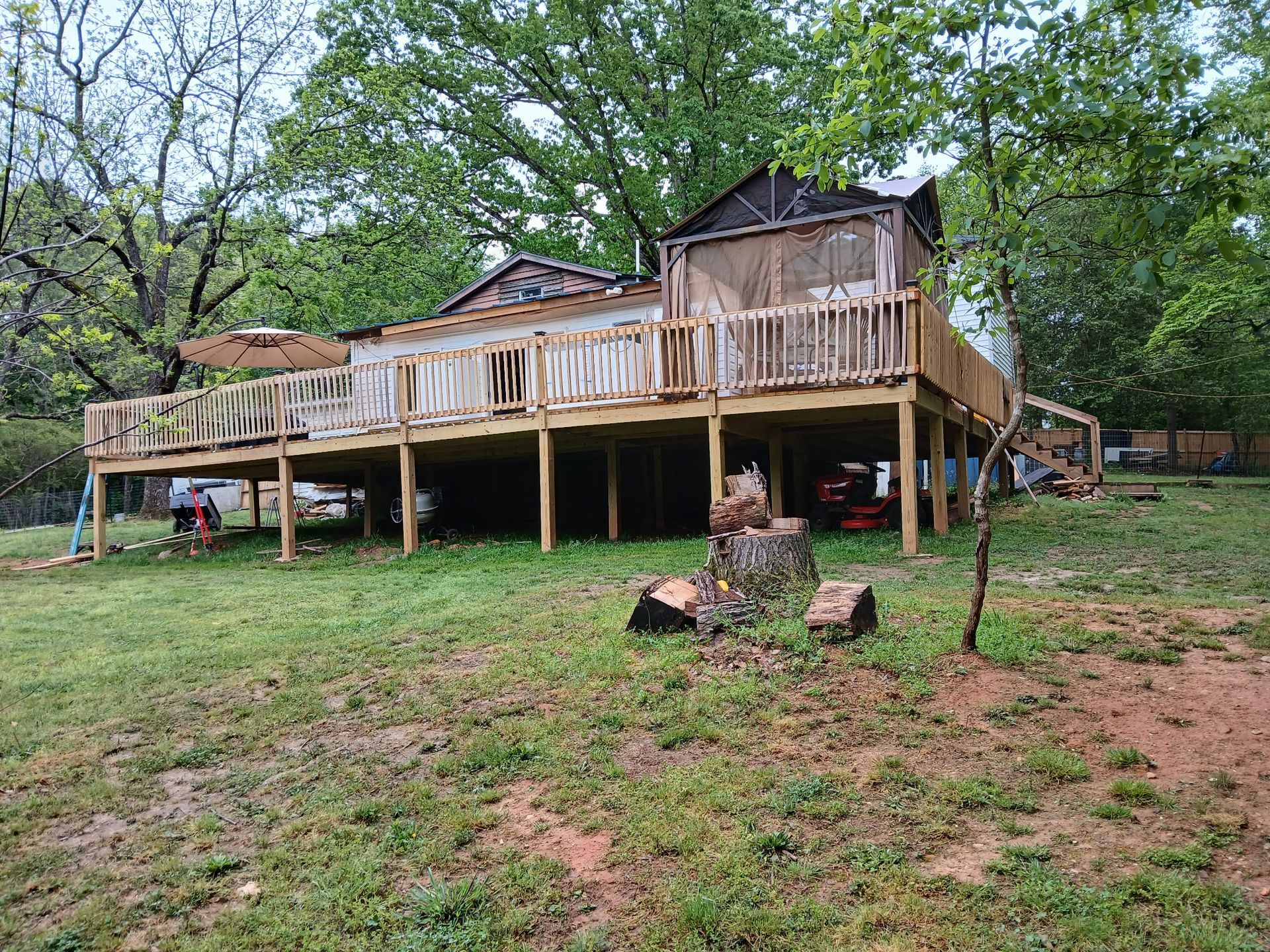 A large wooden deck on stilts, in a grassy yard, with trees in background.