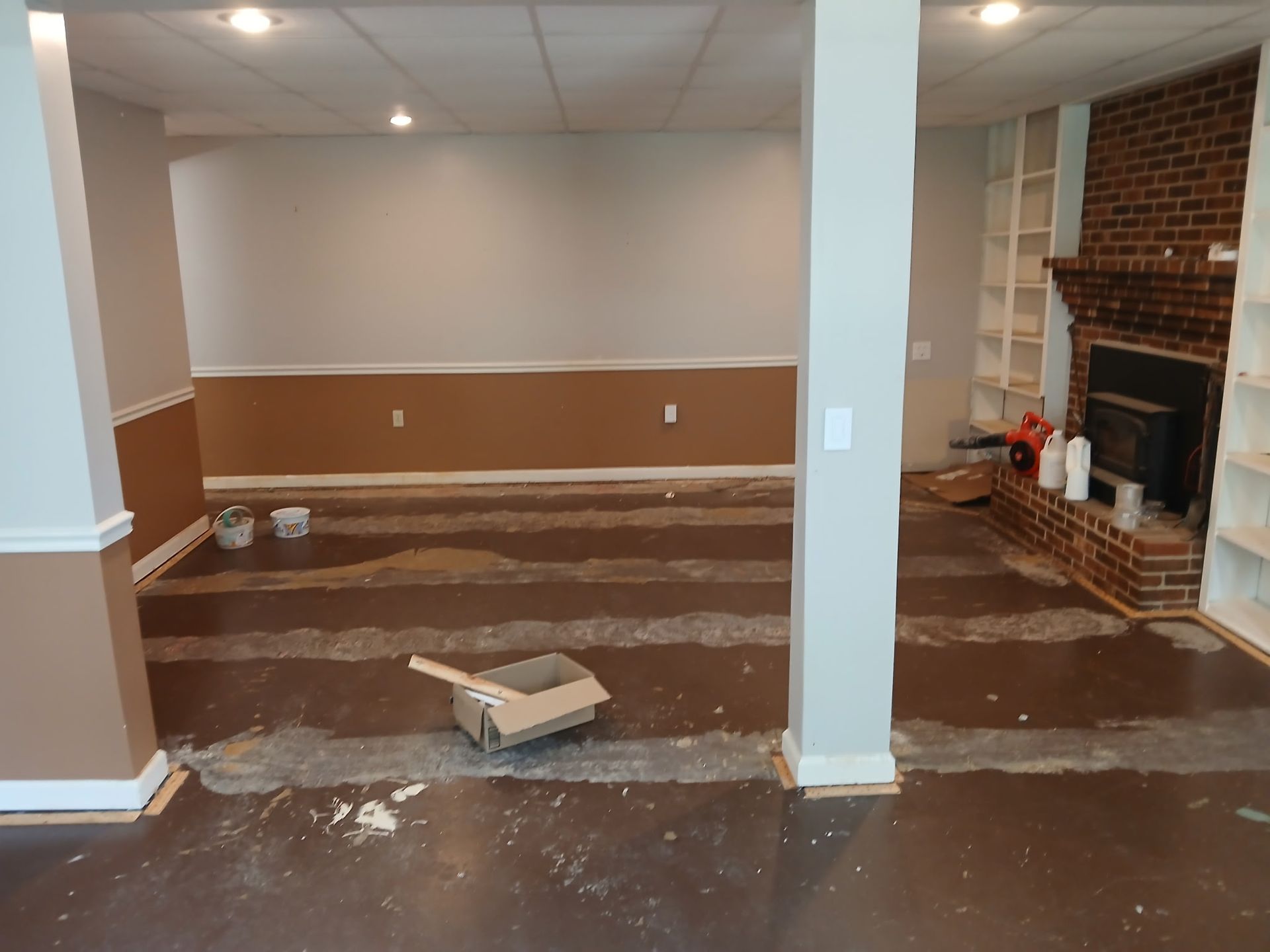 Basement renovation: brown and white walls, exposed floor with concrete, fireplace with bookshelves.