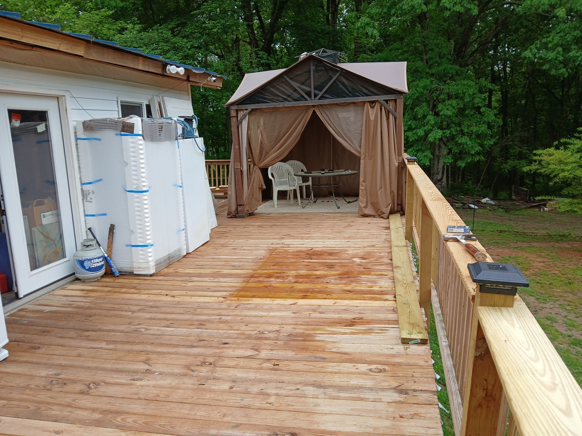 Wooden deck with gazebo, unfinished building. Green trees in the background.