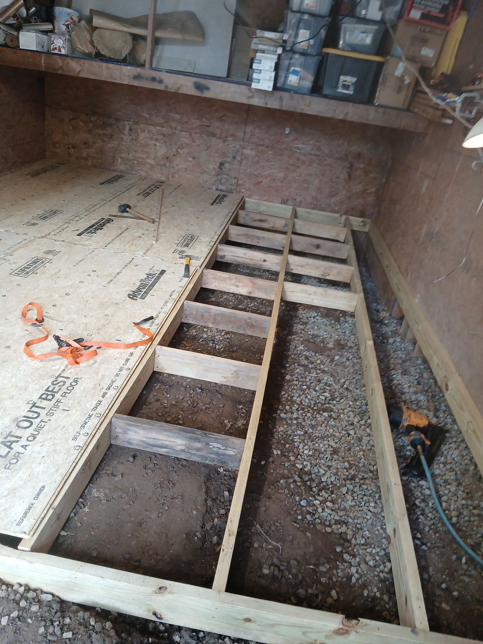 Wooden floor frame under construction in a shed; wood boards and supports in place, ground visible.