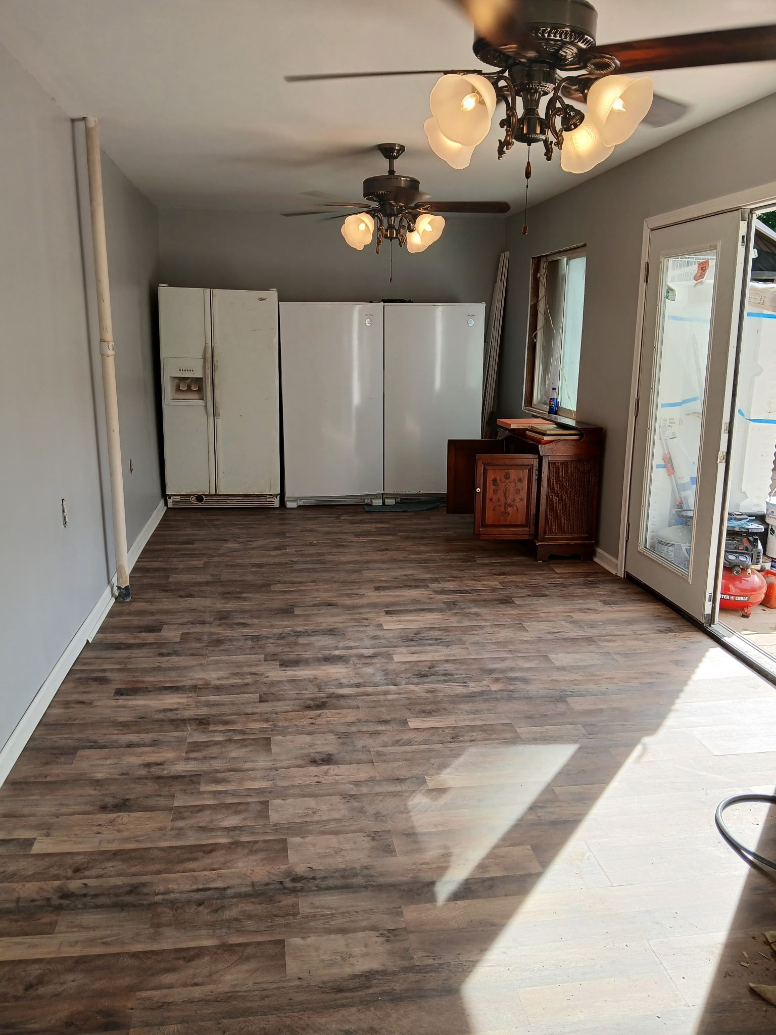 Interior view of a room with wooden flooring, appliances, and a cabinet; French doors on right; two ceiling fans.