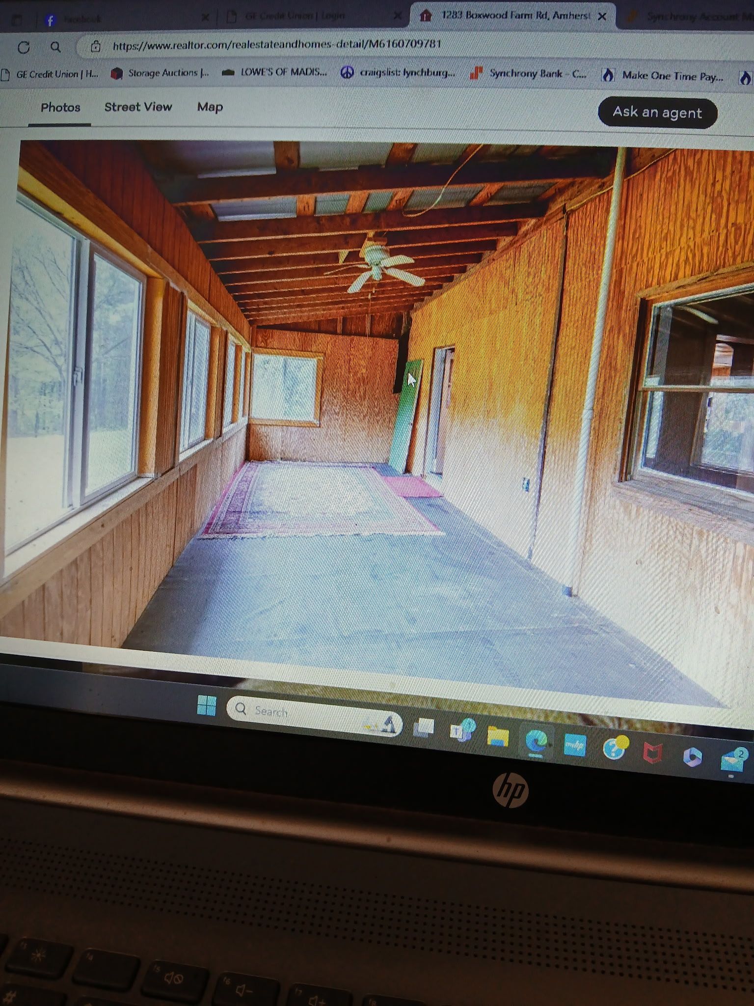 A long, narrow room with wooden walls and ceiling, large windows, and a ceiling fan.