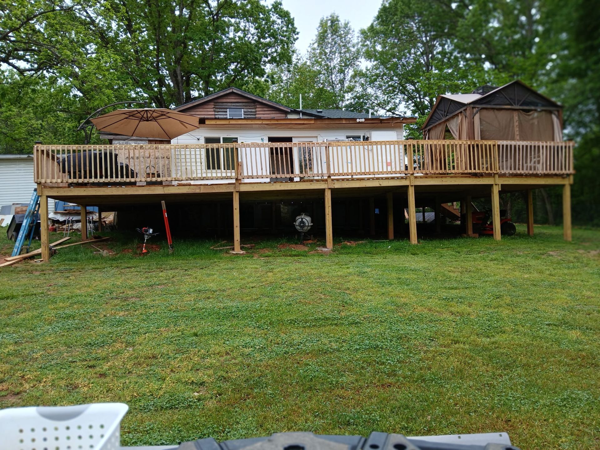 Wooden deck on a white house with a grassy yard and trees in the background.