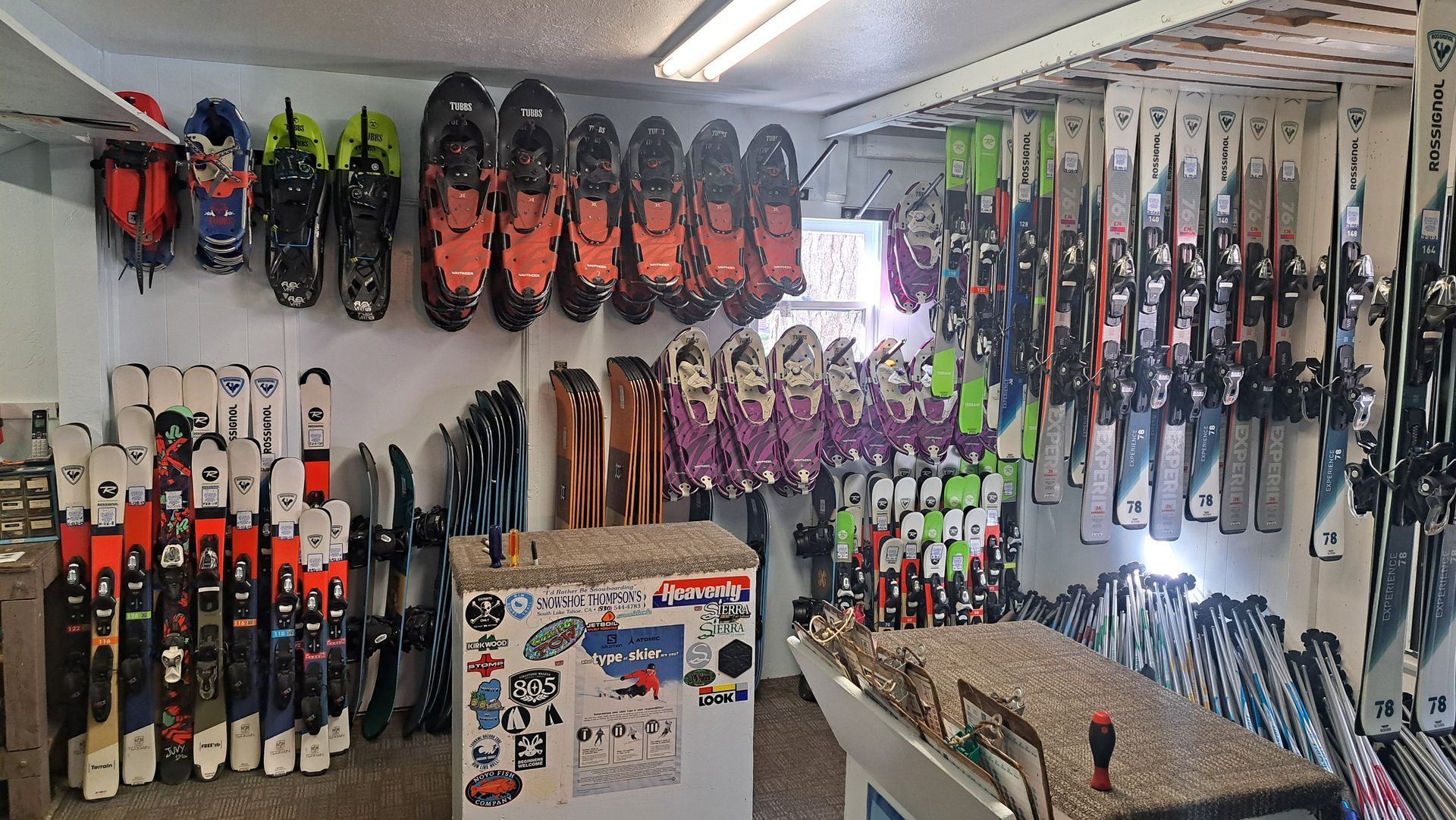 Wall of colorful sports gear and equipment in a shop, with racks of boots, gloves, and skis.