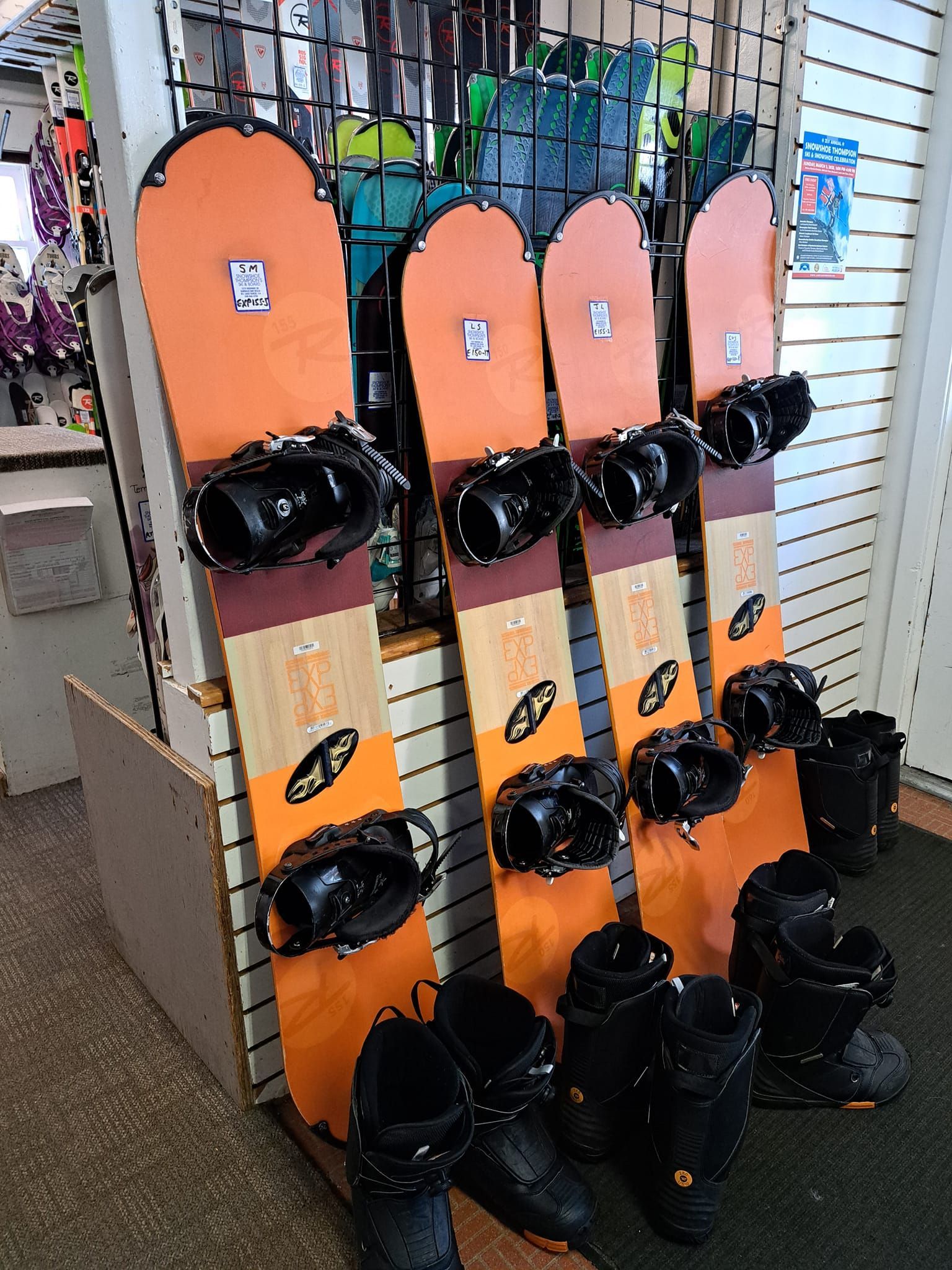 Snowboards and boots displayed in a ski shop, with orange boards and black bindings/boots.