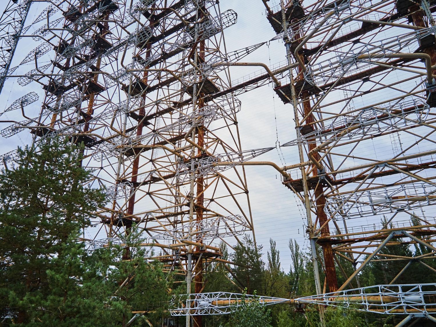 A large metal structure is surrounded by trees and a cloudy sky.