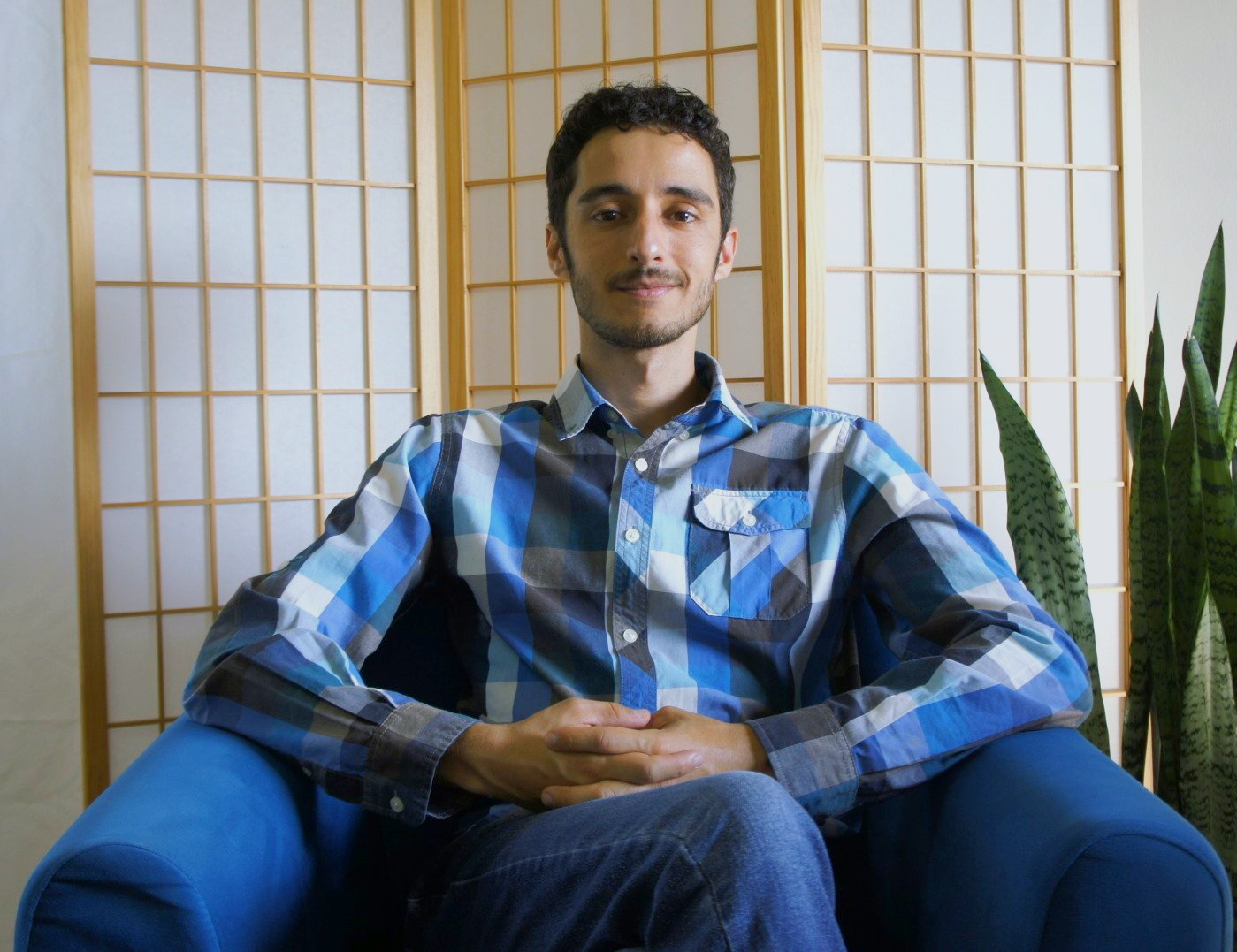 Um homem de camisa xadrez está sentado em uma cadeira azul