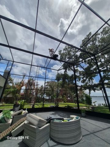 Worker installing a screened pool enclosure beside a backyard swimming pool