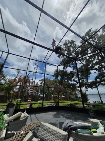 Patio with a black mesh screen roof, cushioned seating, and a green backyard view under cloudy sky