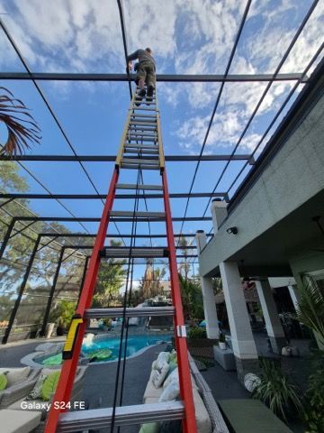 Worker on a red ladder repairing a screened patio roof beside a pool