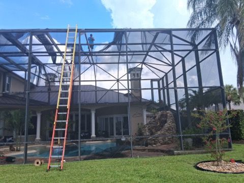 Screen enclosure under construction with a ladder leaning against the frame by a backyard pool.