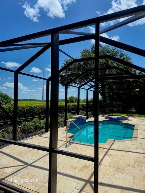 Screened backyard pool and patio with black frame enclosure and turquoise water under a blue sky