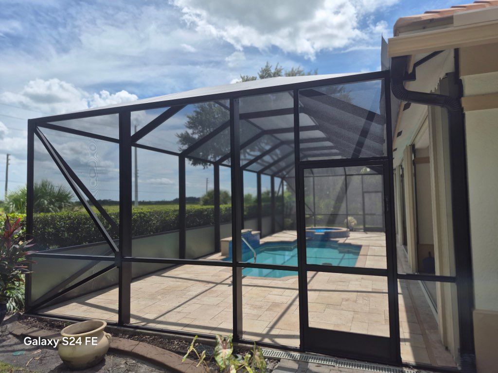 Screened pool enclosure with black frame around a turquoise backyard pool under a partly cloudy sky