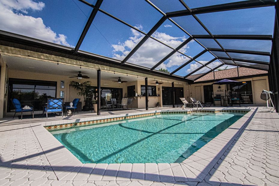 Covered backyard pool with turquoise water, screened enclosure, and patio seating under a blue sky