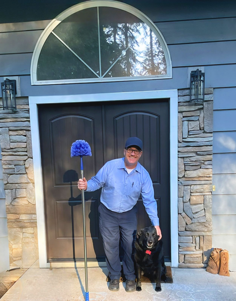 A man standing next to a black dog holding a mop