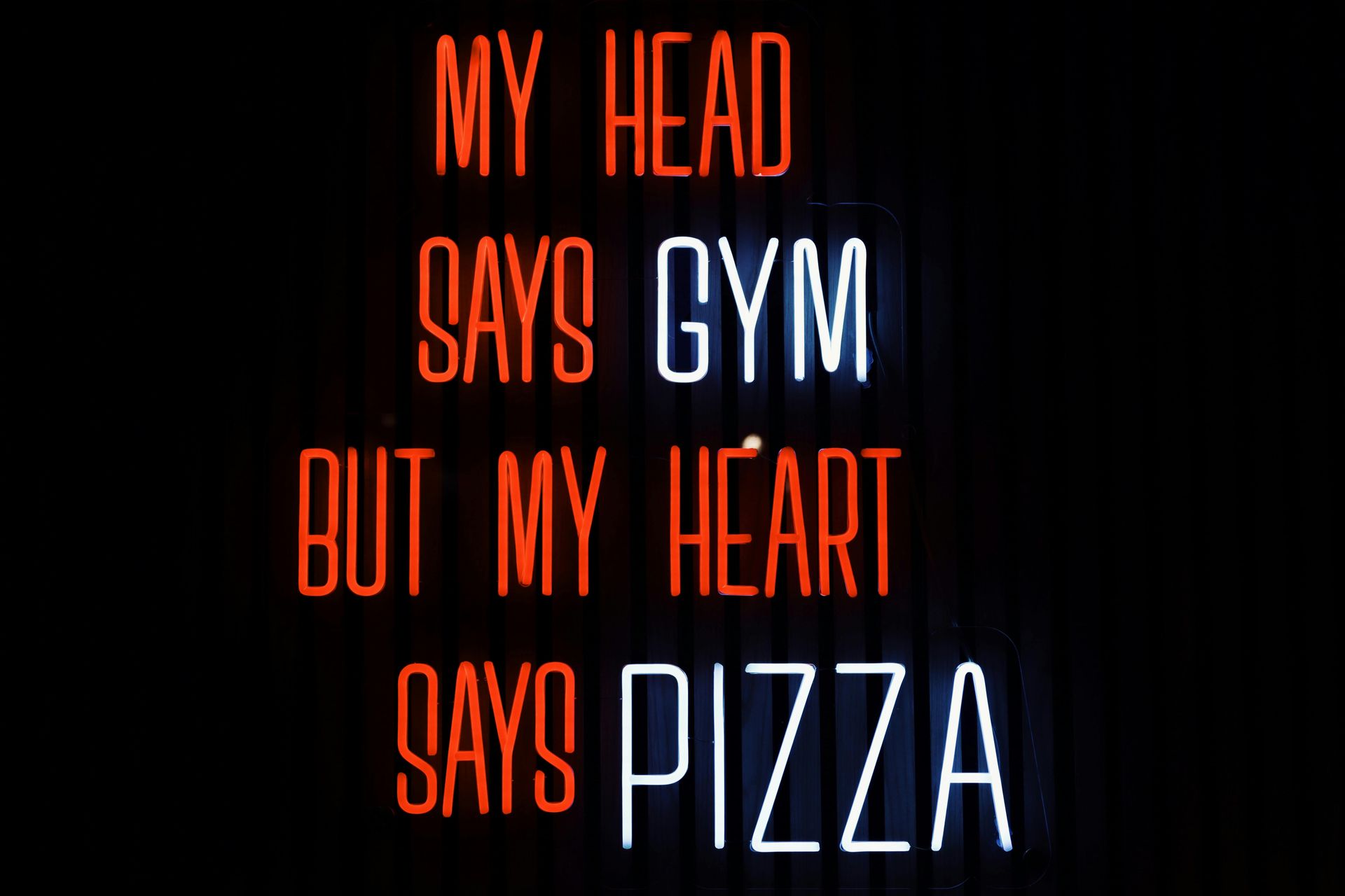 A person is holding a pizza on a wooden cutting board.