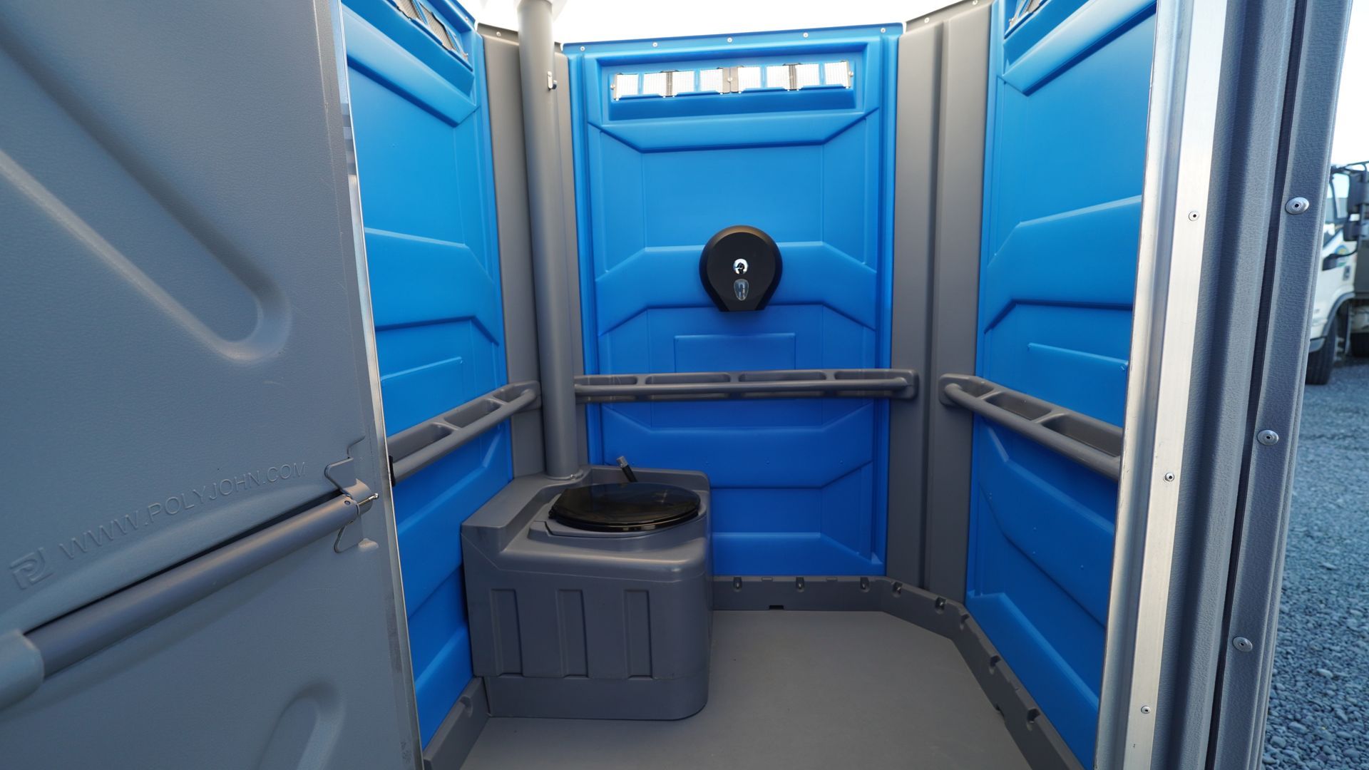 Interior of a blue portable toilet with a toilet seat, showing walls, door and some light.