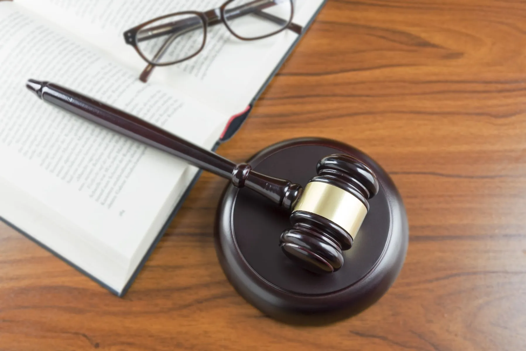 Gavel on wooden sound block; open book and glasses on a table.
