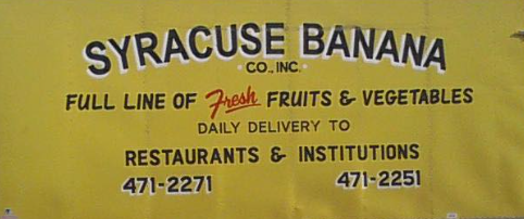 Yellow sign for Syracuse Banana Co., Inc. listing fresh fruits and vegetables with phone numbers.