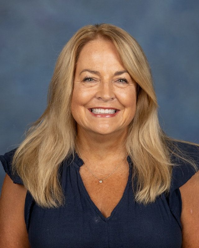 A woman in a white shirt and pearl necklace is smiling for the camera.