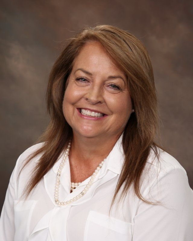 A woman in a white shirt and pearl necklace is smiling for the camera.
