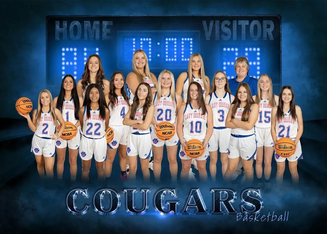 A basketball team is posing for a picture in front of a scoreboard.