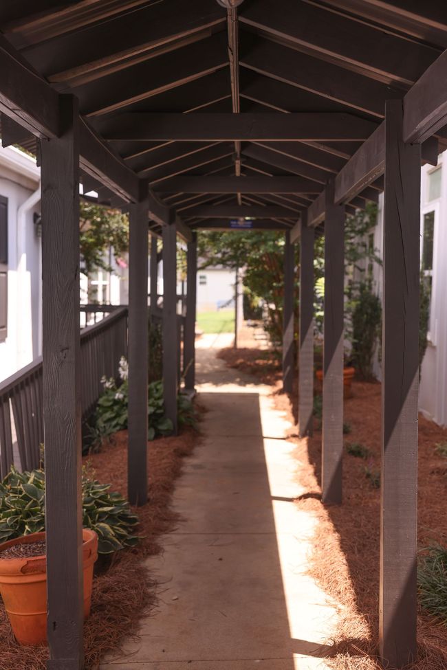 A covered walkway between two buildings with potted plants on the side