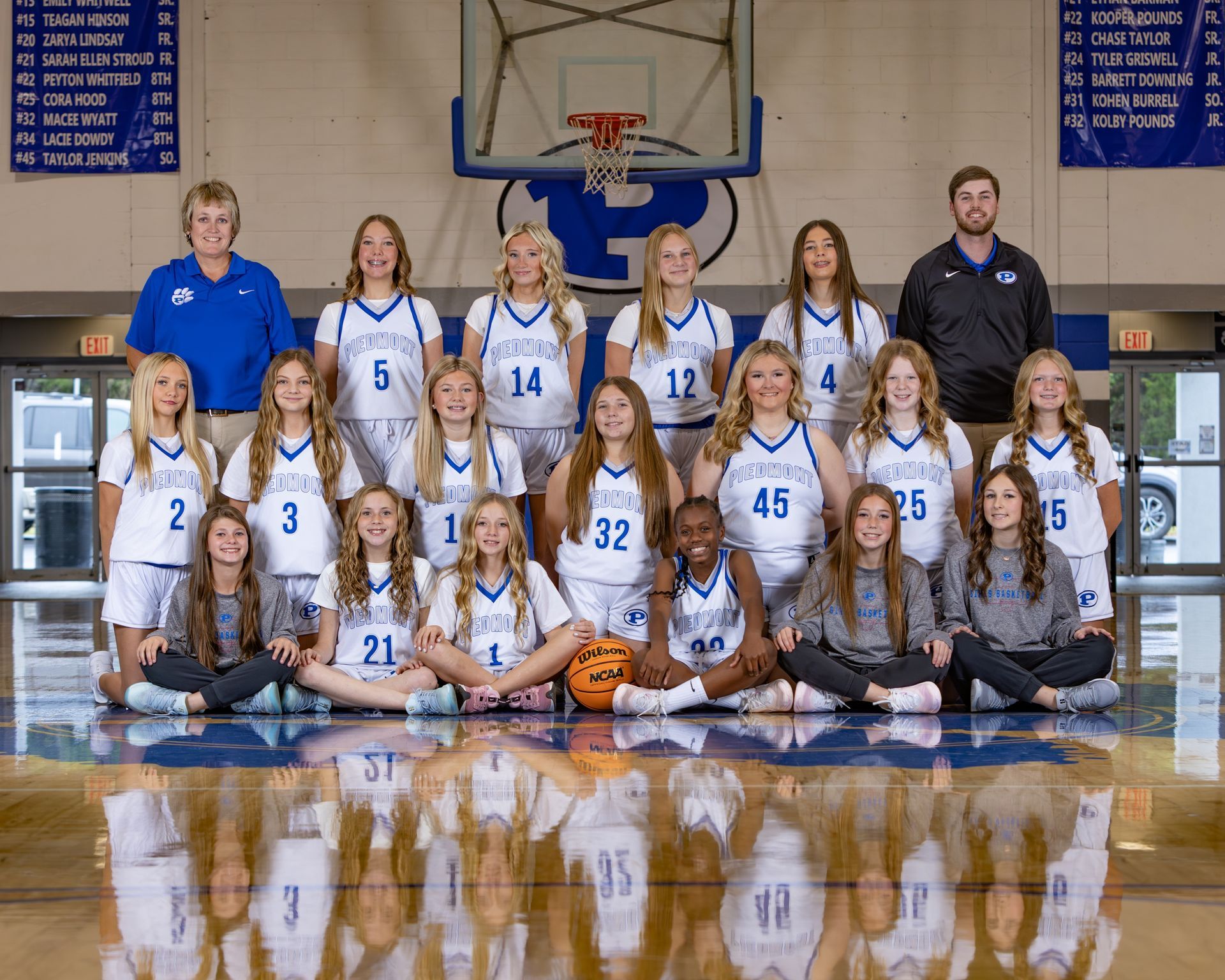 A basketball team is posing for a picture in front of a scoreboard.