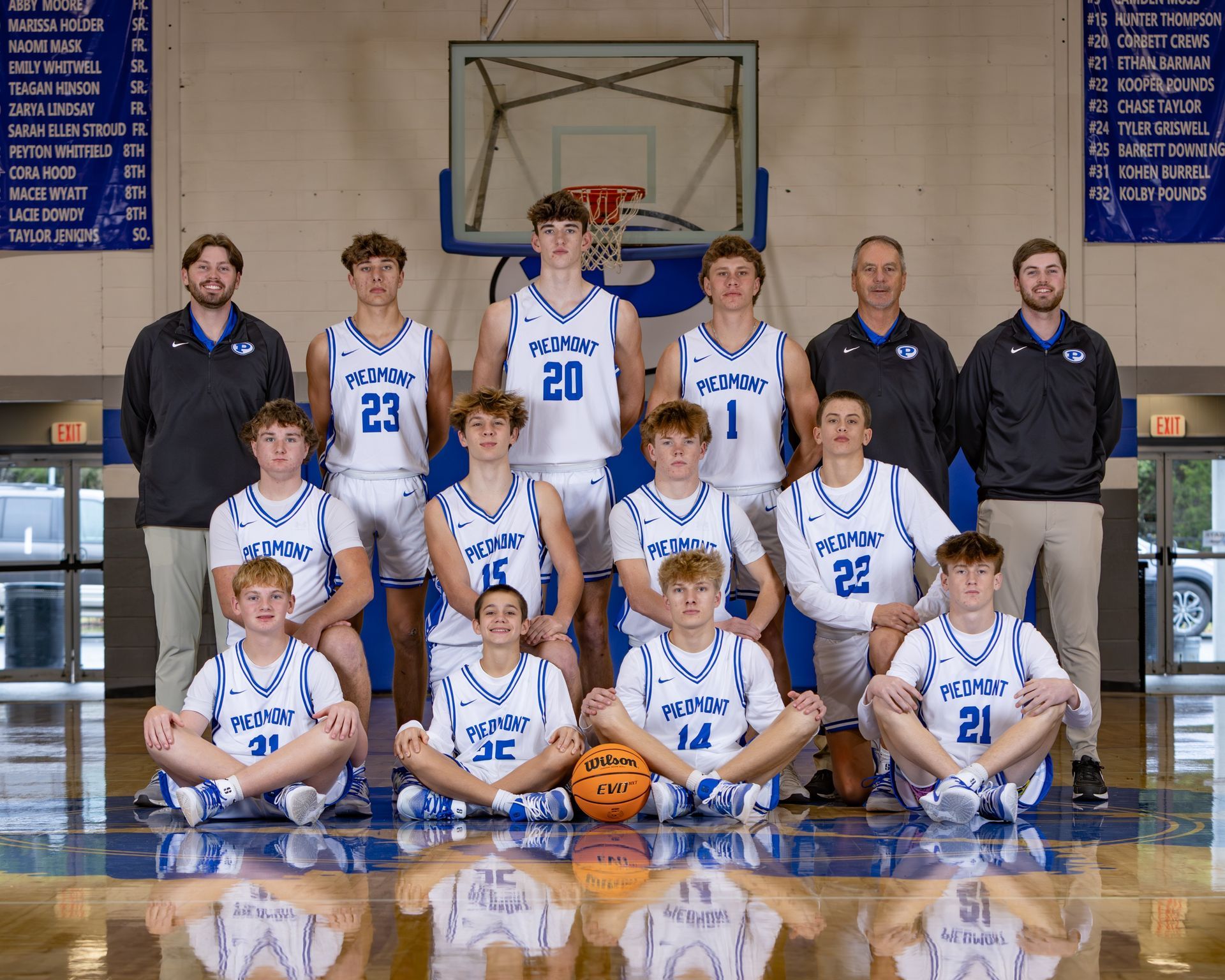 A group of young men are standing next to each other holding basketballs in front of a scoreboard.