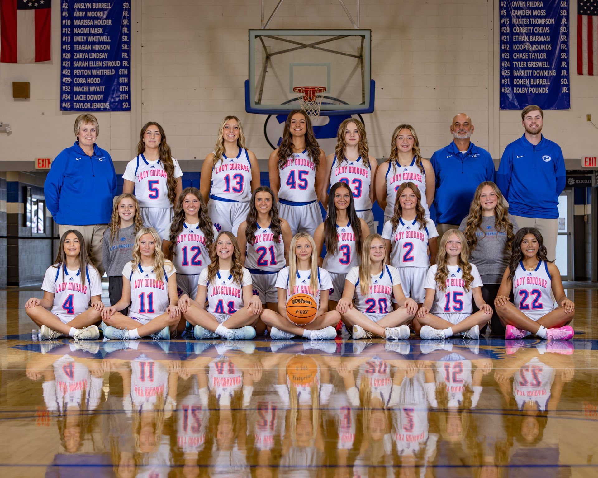 A basketball team is posing for a picture in front of a scoreboard.