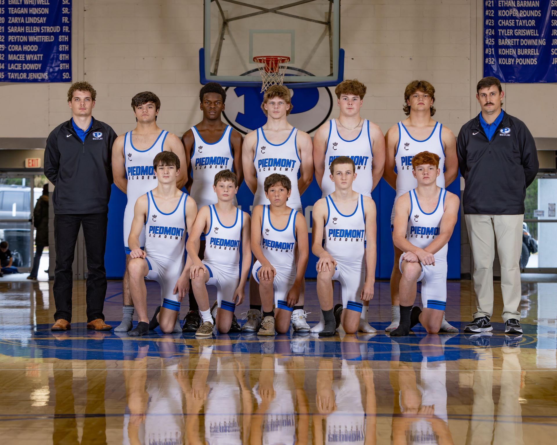 A group of wrestlers are posing for a picture in front of a scoreboard.