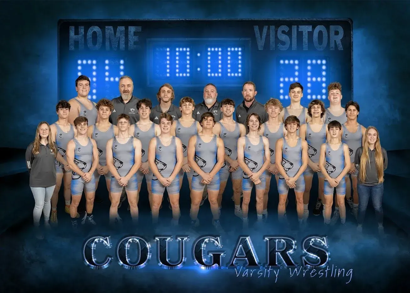 A group of wrestlers are posing for a picture in front of a scoreboard.