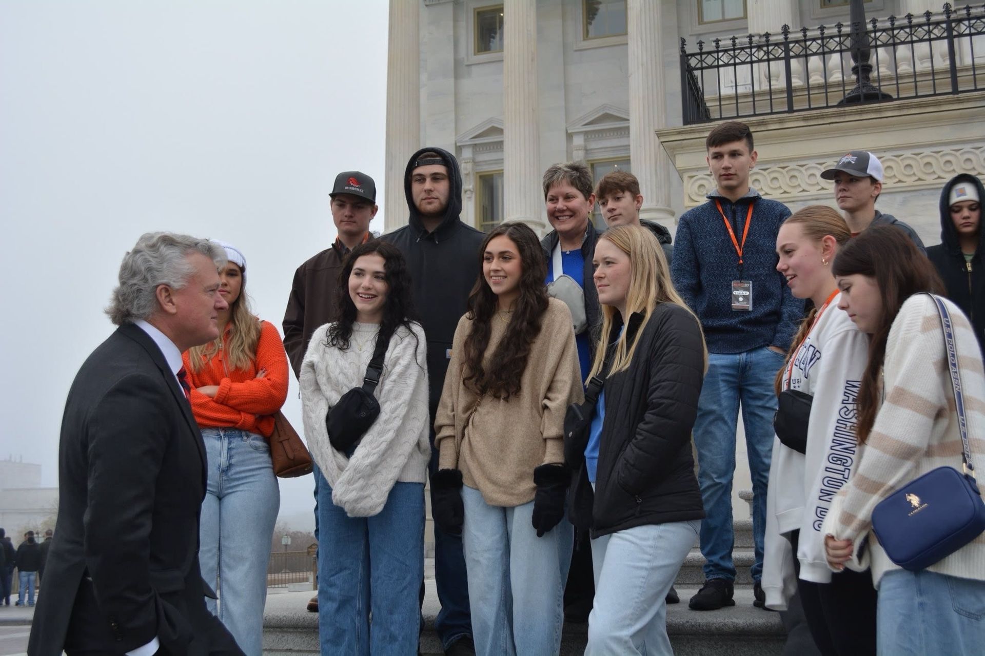 A man in a suit and tie is talking to a group of people standing in front of a building.