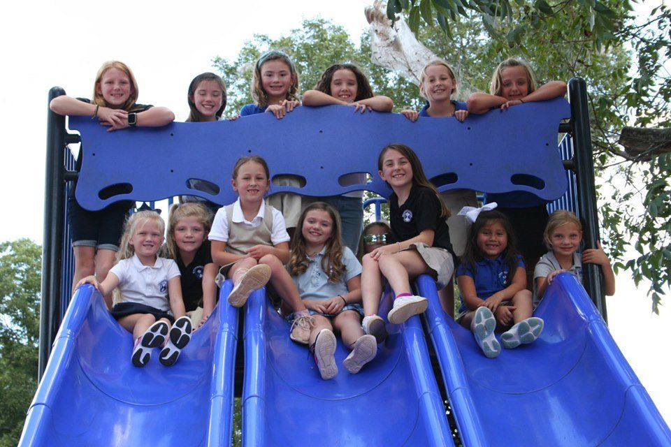 A group of young girls are sitting on a blue slide