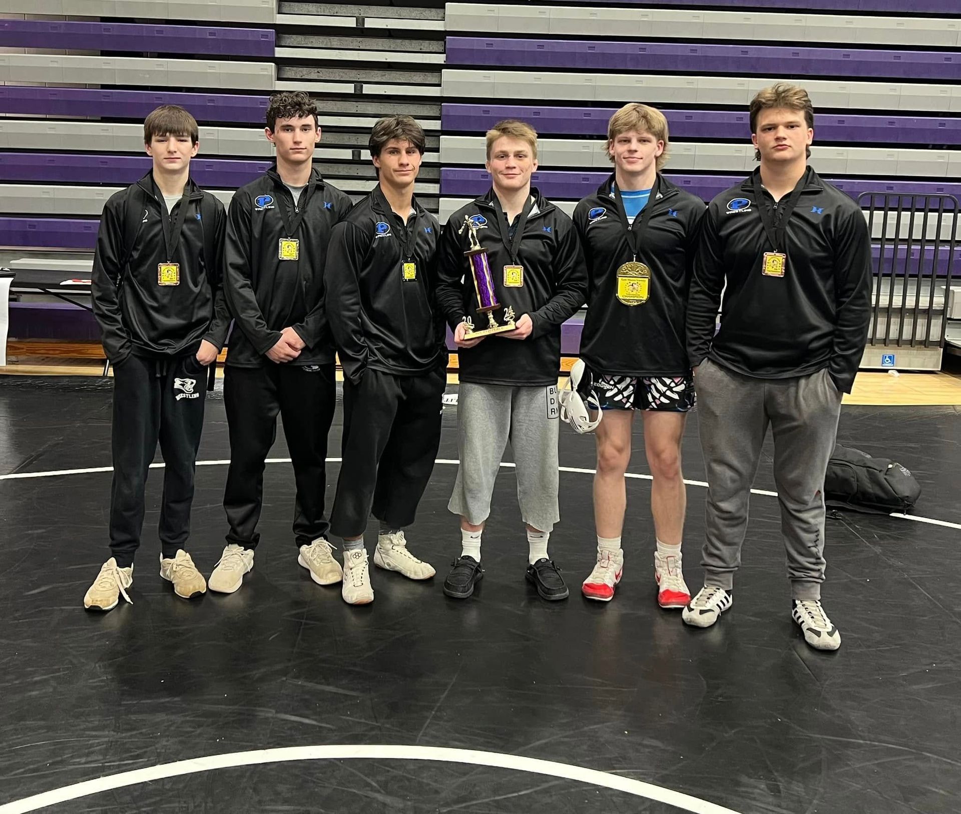A group of young men are posing for a picture on a wrestling mat.