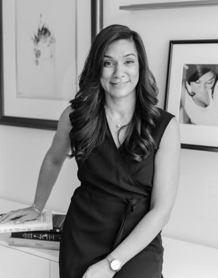 A woman in a black dress is standing in front of a wall with pictures on it.
