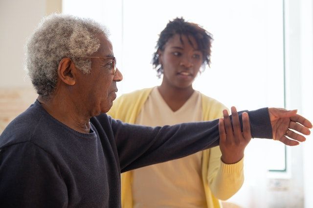 A woman is helping an elderly man stretch his arm.