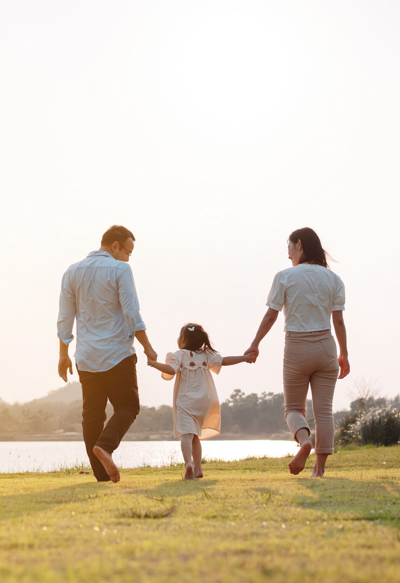 A family is walking across a lush green field holding hands.