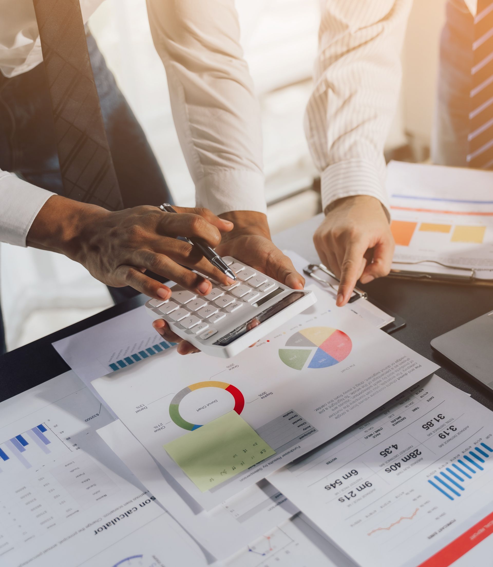 A man is using a calculator while another man looks at a pie chart.