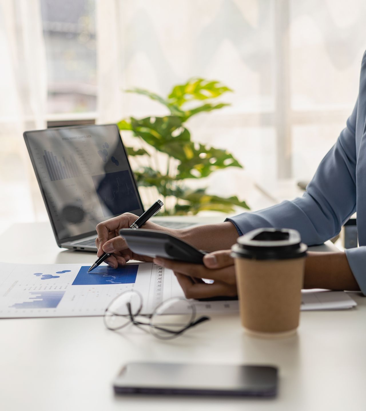 A person is sitting at a desk using a laptop and a cell phone.