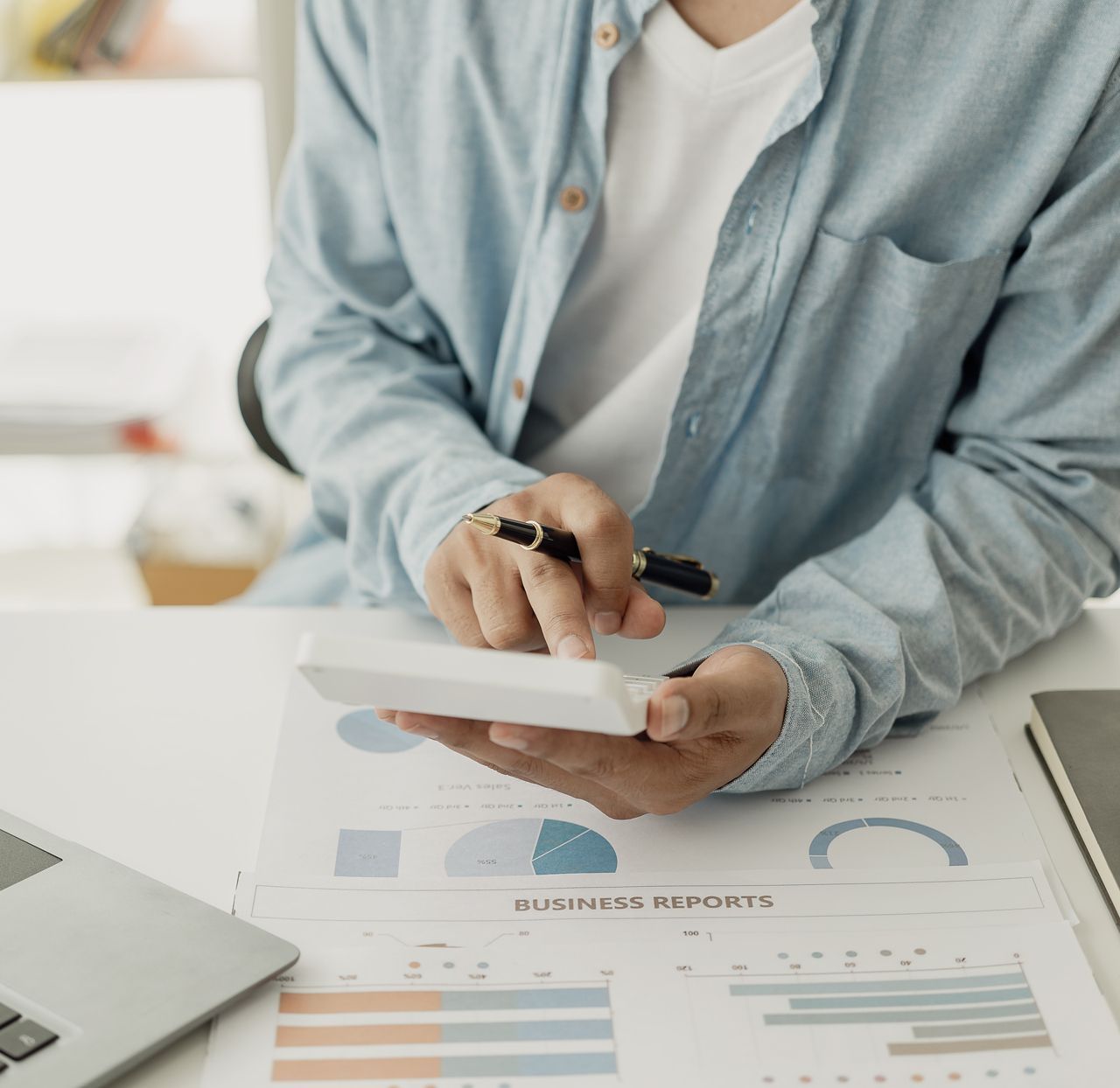 A man is sitting at a desk holding a pen and a notebook with business reports written on it