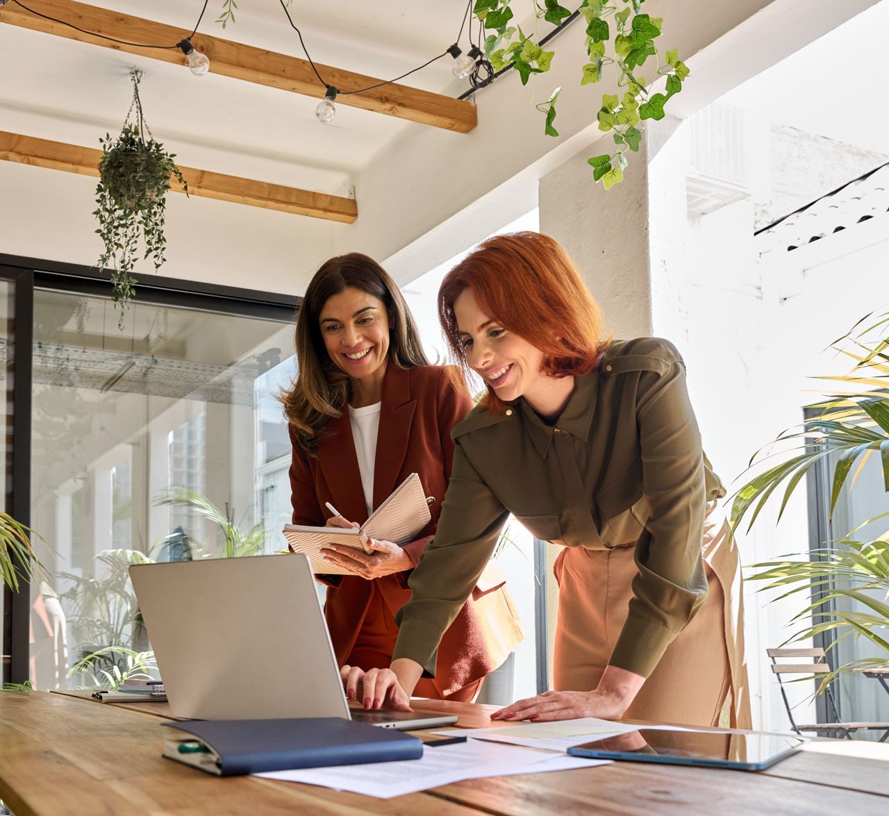 Two women are standing at a table looking at a laptop.