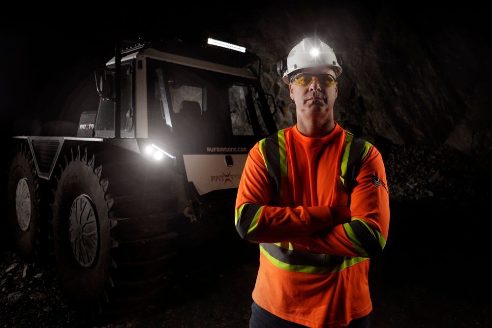 Fat Truck in a mine with a miner standing in front with his safety vest.