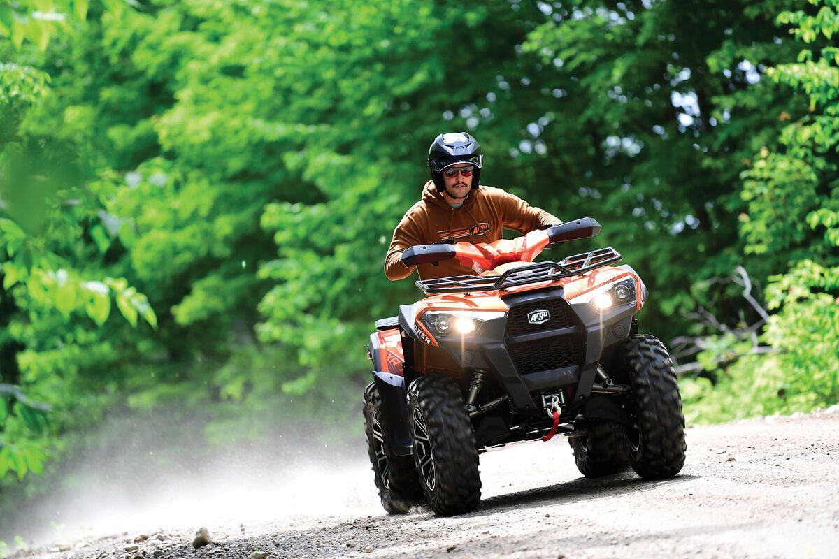 A man in an helmet riding an Argo ATV on a dirt path.