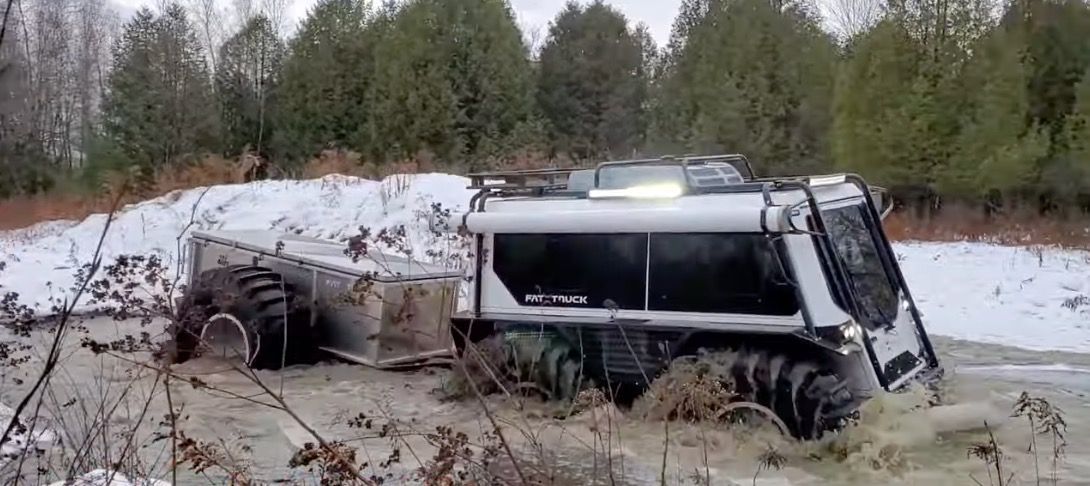 A Fat Truck with its trailer attached moving through deep water.