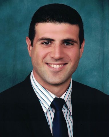 Man in suit and tie smiling, set against a teal-blue backdrop.