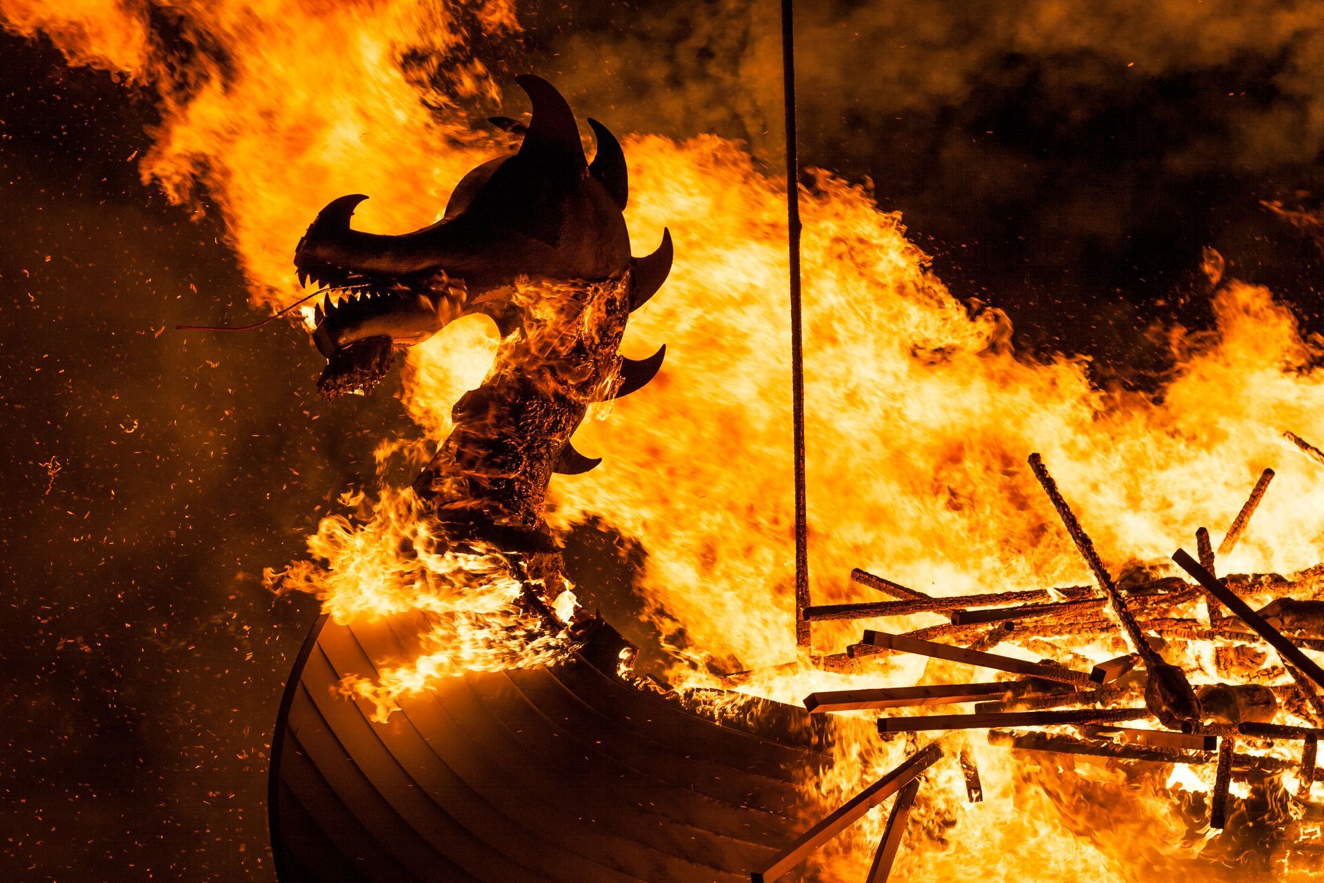 Burning Viking longship, flames engulf dragon-head prow, fiery spectacle, night.