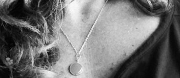 A silver necklace with a circular pendant rests on a person's neck.