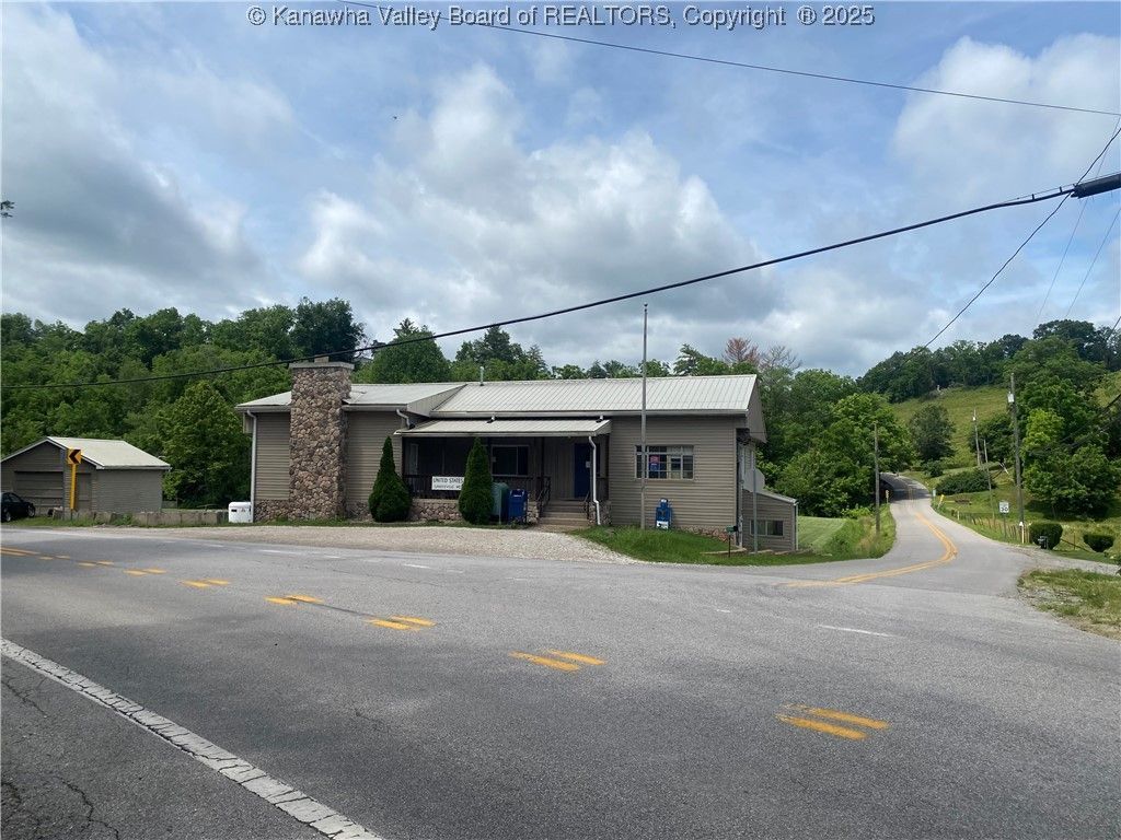 A single-story building with a stone chimney sits at a road intersection under a cloudy sky.