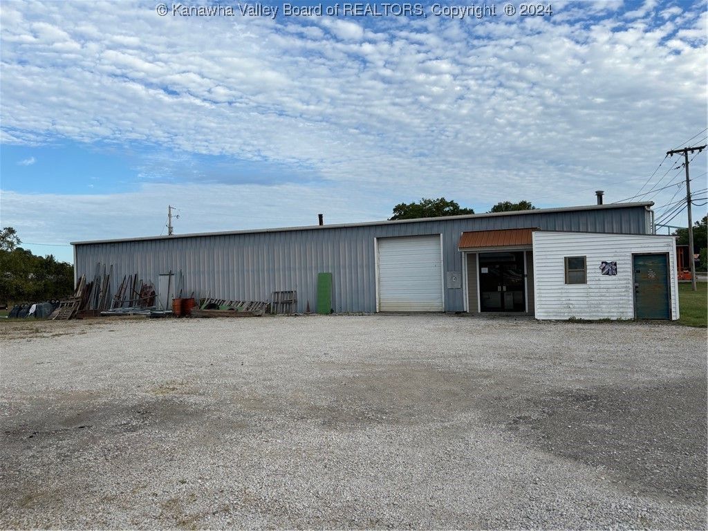Commercial building with metal siding, large garage door, and gravel parking lot under a cloudy sky.